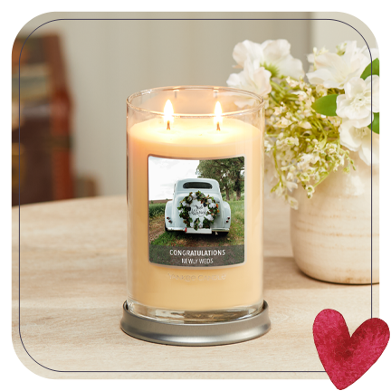 a signature large tumbler candle with a congratulations newly weds personalized photo label on a table next to a vase full of white flowers