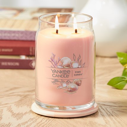 pink sands signature large jar candle on a coaster next to a stack of books on a wood table